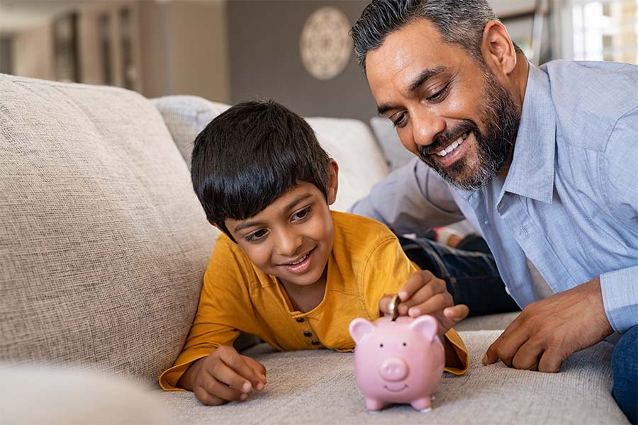 Money Savings Checklist - Closeup Portrait of a Smiling Father Watching His Son Put Coins in a Piggybank at Home